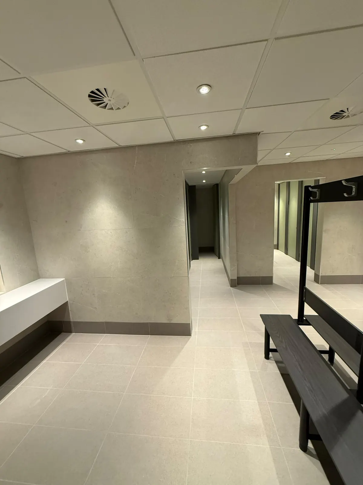Changing room with bench seating and coat hooks against Unika Light 600 × 600 walls, on EXT Core Grey floor tiles