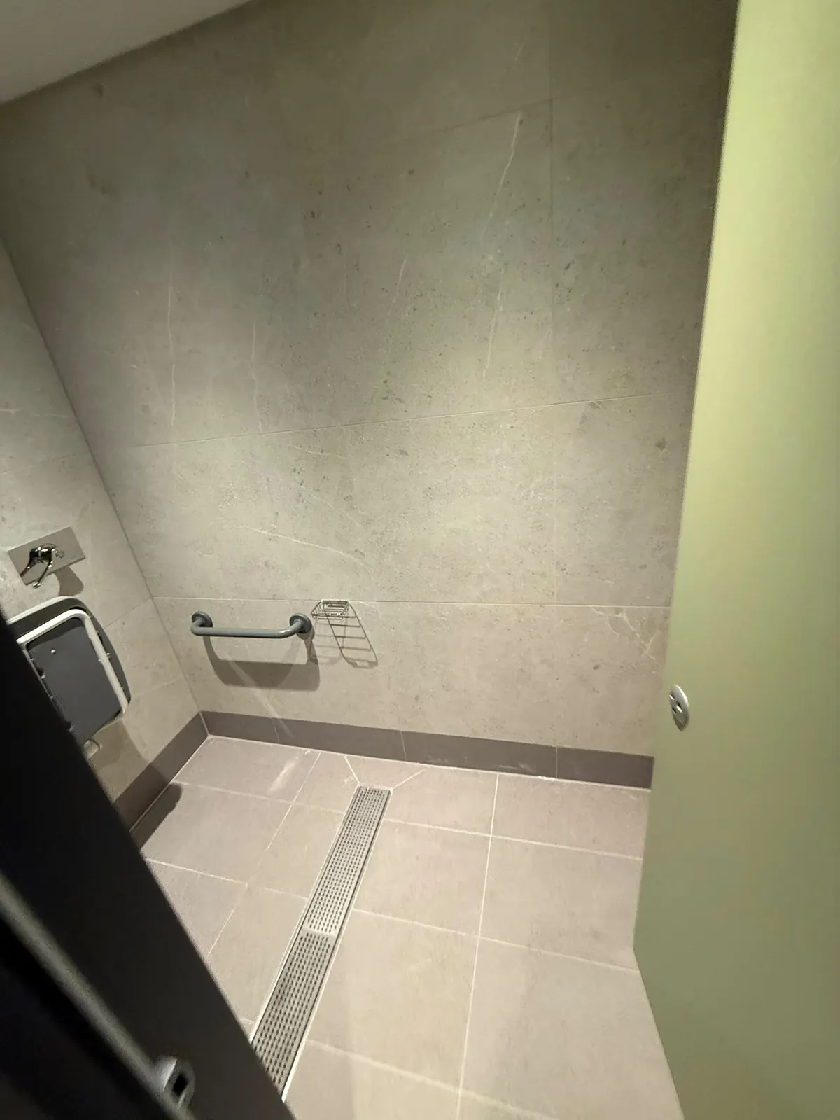 Shower area with a stainless linear drainage channel, grab rail and soap basket, the floor laid to falls