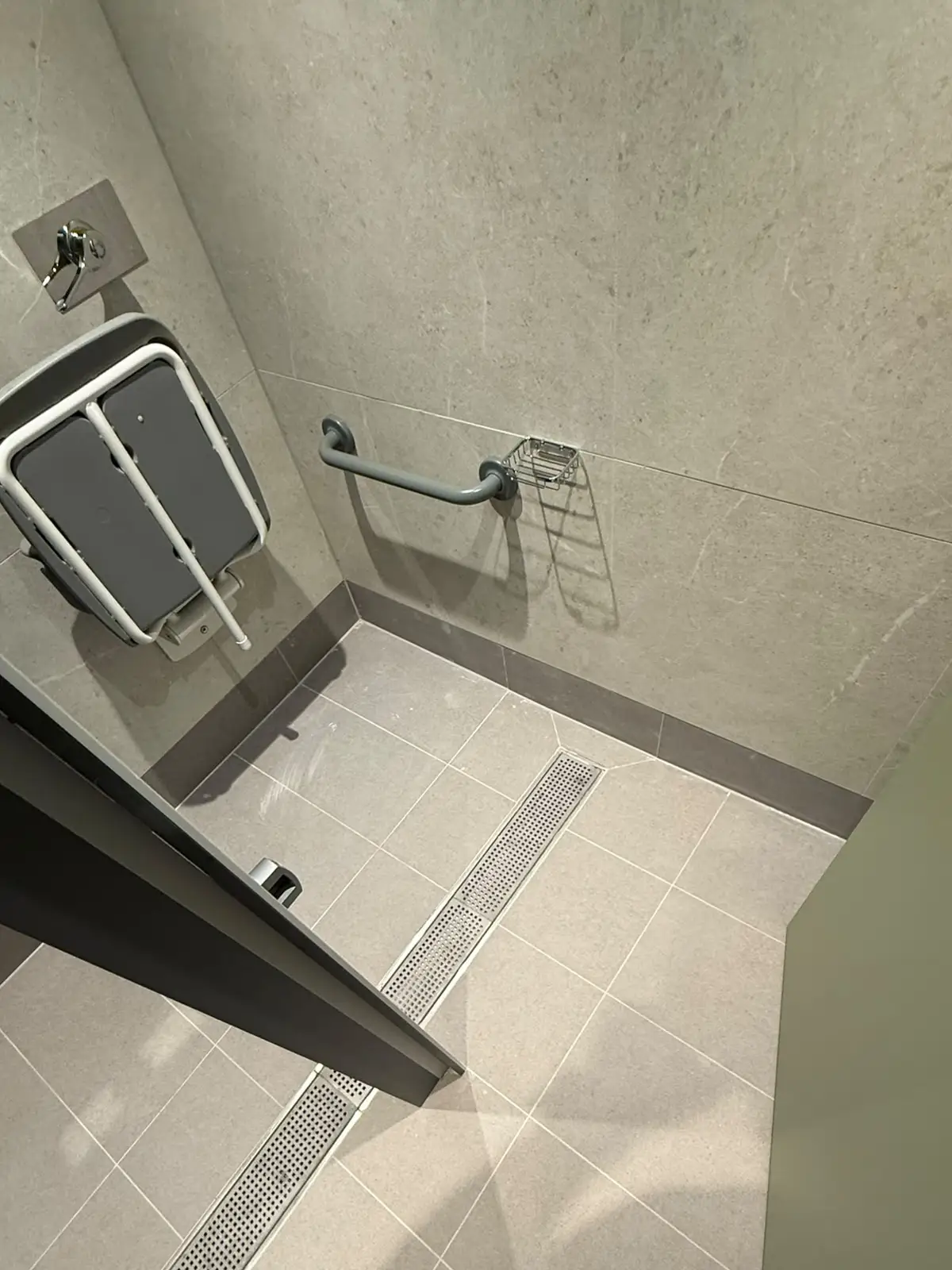 Accessible shower with a drop-down seat and grab rail, the floor laid to falls towards a linear drainage channel