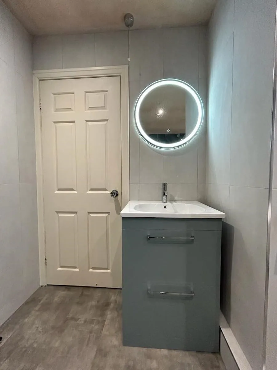 Vanity unit and round lit mirror against light grey wall tiles