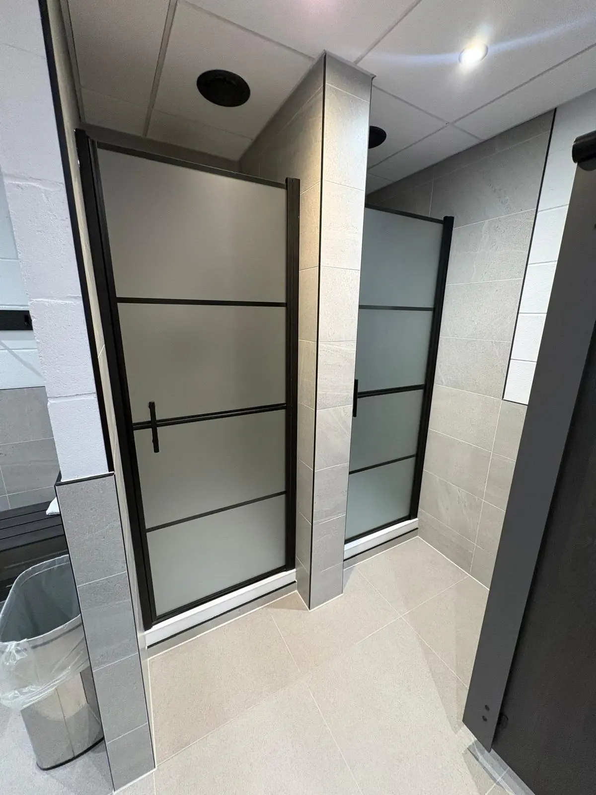 Two shower cubicles with full-height Soft Spartia Perla walls and black metal trims on every corner