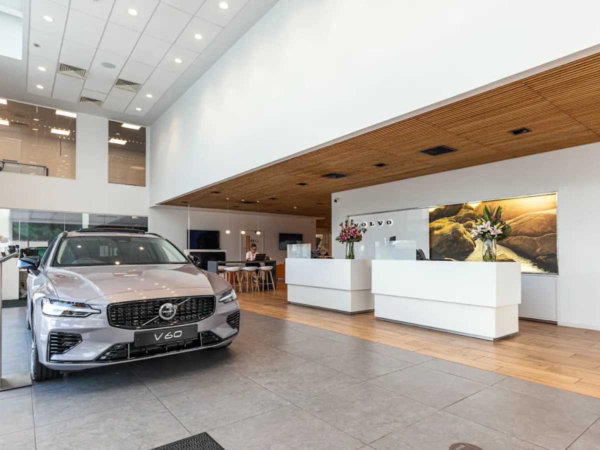 Car dealership showroom with a large-format grey porcelain floor meeting wood-effect tiles at the reception desks
