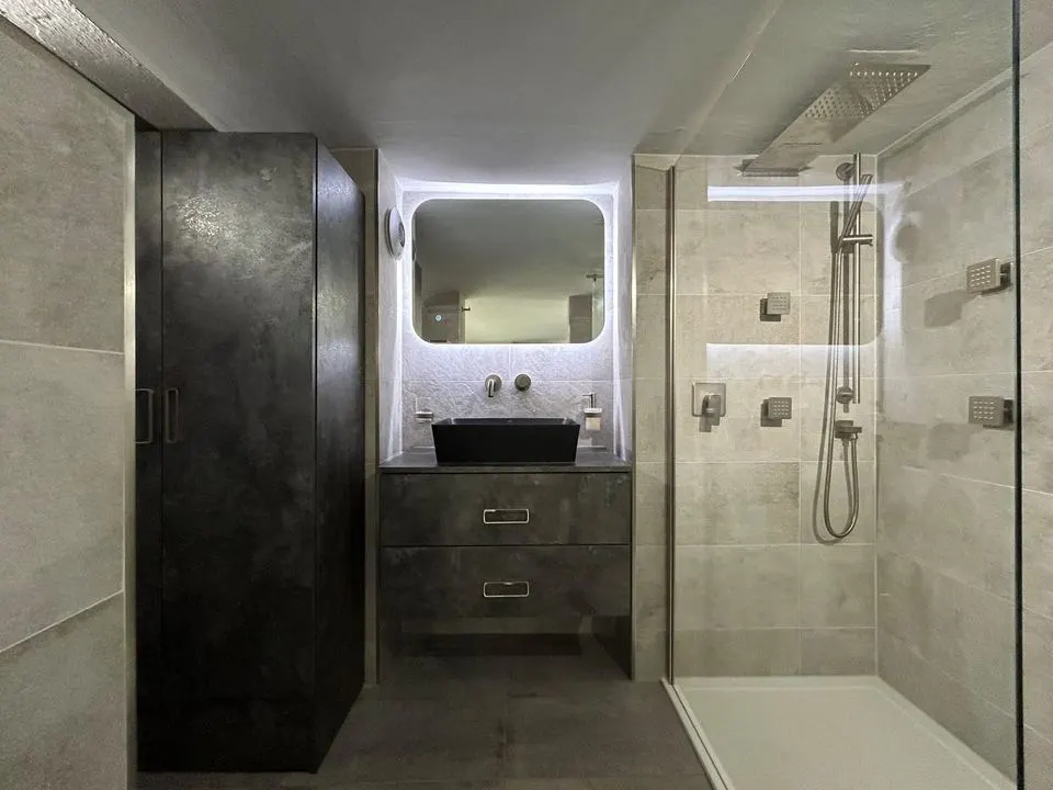 Finished bathroom with grey porcelain walls, a walk-in shower and a lit mirror