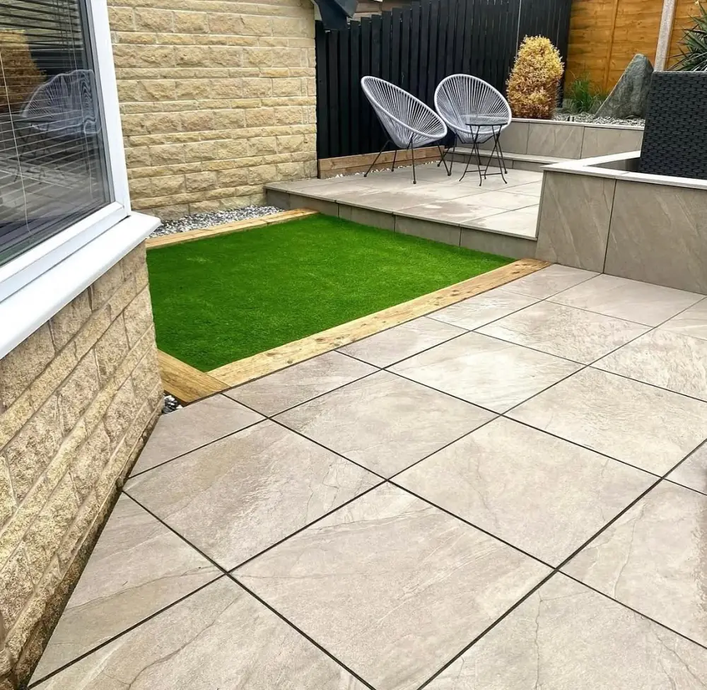 Outdoor porcelain patio wrapping a lawn, with a raised tiled seating area beyond