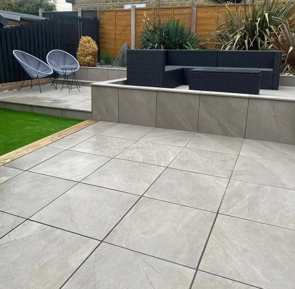 Large-format outdoor porcelain patio below a raised tiled terrace with rattan seating